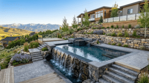 A modern custom swimming pool built on a steep hill in Park City, Utah, featuring cascading retaining walls and an infinity edge overlooking mountains. This image illustrates how expert design can turn terrain challenges into luxurious features